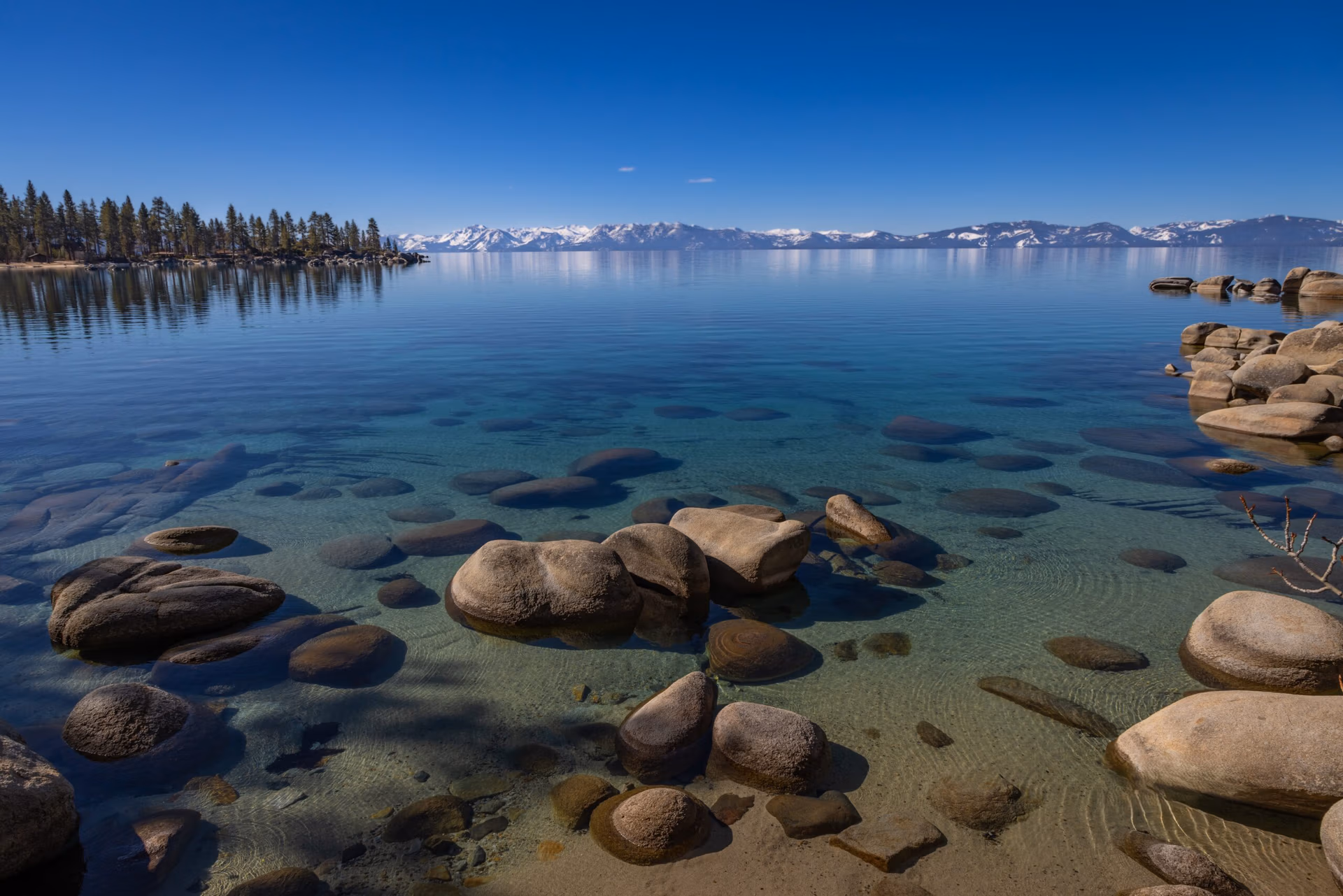 Clear Lake Tahoe water with shoreline stones and Sierra Nevada mountains in the distance.