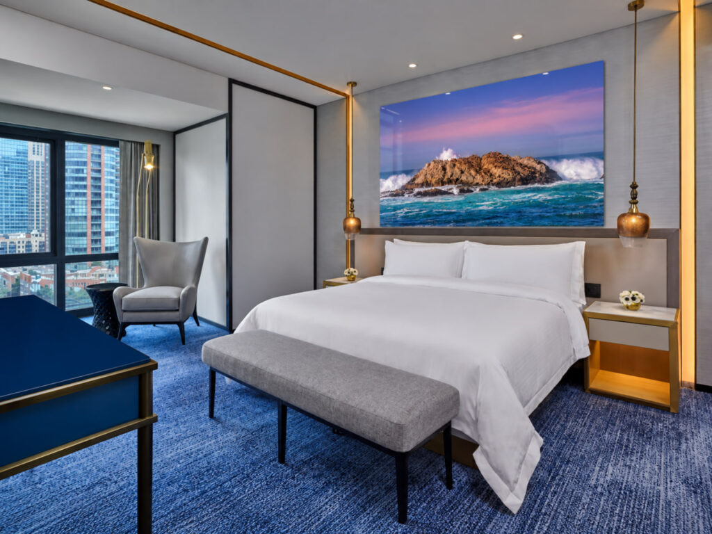Contemporary hotel guest room with large acrylic ocean landscape artwork above the bed.